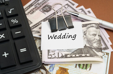 On a brown background lies a calculator and dollars on a clip with an inscription on paper - Wedding