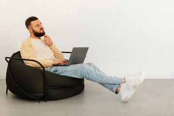 Thoughtful Man Using Laptop Thinking Sitting In Chair At Home