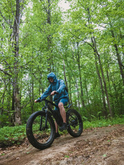 An adult man rides down the mountain on an electric fatbike on a dirt road. Healthy sports hobby in nature.