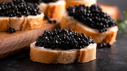 Slices of bread with black caviar on rustic dark background