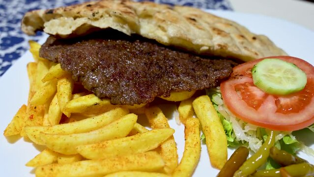 Burger served on plate in restaurant. Traditional meat dish. Meat prepared on barbecue and served with bread, potatoes and salad. 