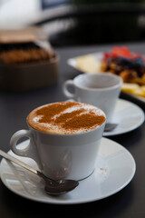 Traditional Italian breakfast. Small white ceramic cups with espresso coffee and cappuccino on a table with saucers and metal spoons at a local bar (European coffee shop) in Milan, Lombardy, Italy. 