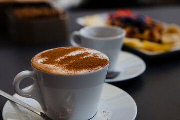 Traditional Italian breakfast. Small white ceramic cups with espresso coffee and cappuccino on a table with saucers and metal spoons at a local bar (European coffee shop) in Milan, Lombardy, Italy. 