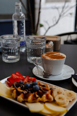 Traditional Italian breakfast. Fresh classic waffles with fruits, sugar powder, chocolate and cappuccino coffee with cinnamon in Milan, Lombardy, Italy. European food, drinks  pastry at a local bar.