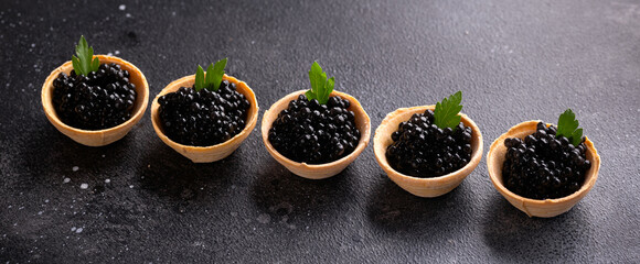 Tartlets with black caviar on rustic background