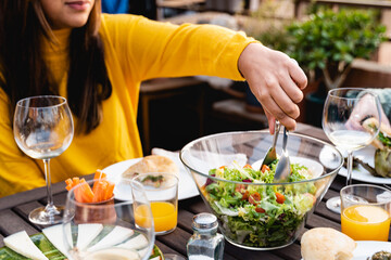 Happy people eating vegan food dinner outdoor at patio restaurant - Focus on african woman hand