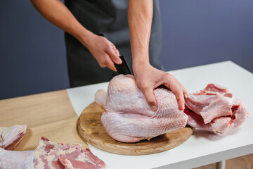 Male hands cut the carcass of a large Turkey on a wooden board. Fresh meat.