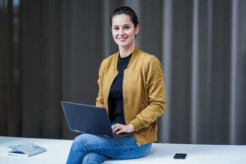 happy smiling remote working woman in casual outfit sitting in cross legs pose with her laptop or...