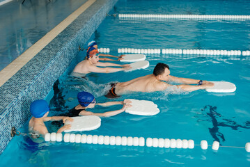 A group of boys and girls train and learn to swim in a modern swimming pool with an instructor. Development of children's sports. Healthy parenting and promotion of children's sports.