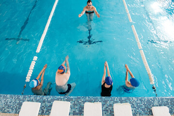 A group of boys and girls train and learn to swim in a modern swimming pool with an instructor. Development of children's sports. Healthy parenting and promotion of children's sports.