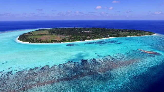 Aerial fly back of small island with houses, ocean skyline and deep water, Maldives atoll with houses and tropical forest. Concept of traveling
