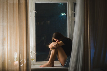 Sad woman sit barefoot on window sill