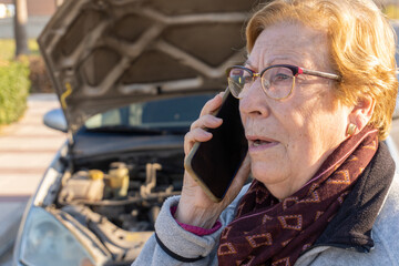 Senior woman with broken down car calling and asking for help from vehicle assistance and rescue service.