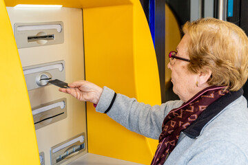 Elderly woman with a credit card at an ATM. - obrazy, fototapety, plakaty