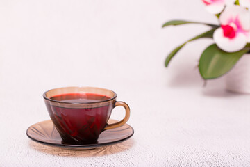 Flower tea karkade. Delicious herbal tropical drink on a bright table. A cup of pink tea from dry hibiscus petals, a natural medicinal drink against the background of fern leaves. Tropical morning.