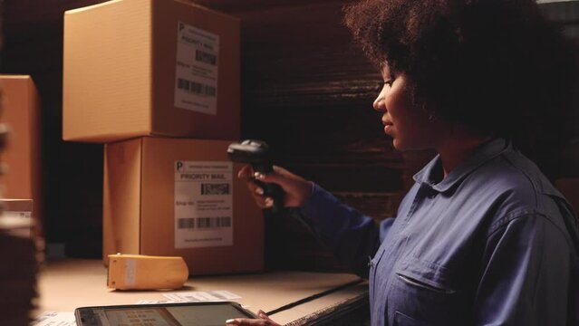 African American worker  working in storage, taking parcel and scanning barcode. Female business person at workplace in warehouse, concept of delivering and logistics. Businesswoman owner.