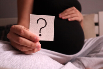 A pregnant woman is holding a card with a question mark. Photo for gender party