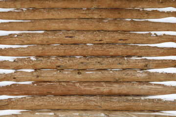 A wall made of wooden logs, covered with snow.