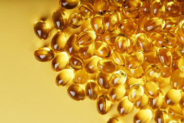 Pile of golden capsules of vitamin D3 on a yellow background with free space