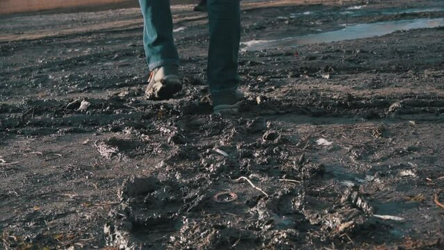 Man in boots walks through the mud, splashing from a puddle in slowmo. A guy in dirty shoes walks down the street. Rainy weather, slush. Close-up of a man's legs walking in a swampy area.