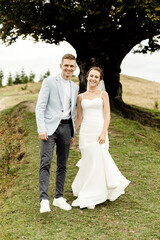 a cheerful wedding couple walks under a large and beautiful branchy tree in the mountains. wedding day