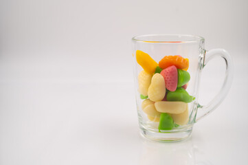 Colorful jelly candies in a transparent glass cup on a white isolated background. Copy space.