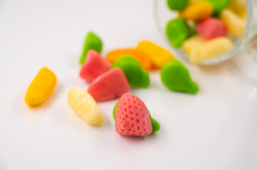Close-up of a pile of a colorful jelly candies spilled out from an overturned glass cup on a white isolated background.