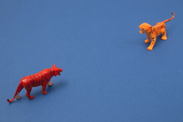 Two tigers facing each other, on a blue background. Minimal animal scene. - Powered by Adobe
