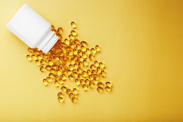 Gold Vitamin D3 capsules poured out of a jar on a yellow background with free space