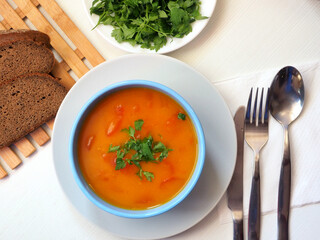 Pumpkin soup with herbs, cutlery, bread, parsley leaves. Flat lay