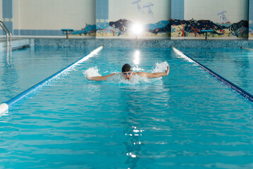 A young man trains and swims in a modern swimming pool. Sports development. Preparation for...