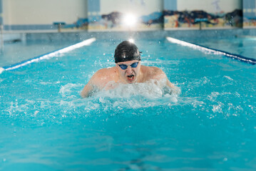 Fototapeta na wymiar A young man trains and swims in a modern swimming pool. Sports development. Preparation for competitions, and a healthy lifestyle. Water treatments and a healthy lifestyle.
