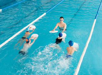 A group of boys and girls train and learn to swim in a modern swimming pool with an instructor. Development of children's sports. Healthy parenting and promotion of children's sports.