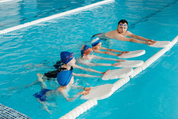 A group of boys and girls train and learn to swim in a modern swimming pool with an instructor. Development of children's sports. Healthy parenting and promotion of children's sports.