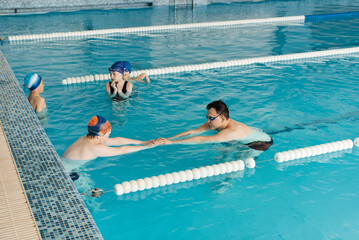 A group of boys and girls train and learn to swim in a modern swimming pool with an instructor. Development of children's sports. Healthy parenting and promotion of children's sports.