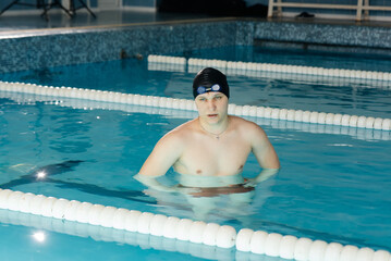 A young man stands and prepares for a workout in a modern swimming pool. Training and sports...