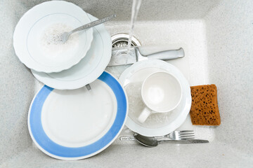 Dishwasher full of dirty dishes. Washable dishes in the sink. Dishes are ready for washing. Water flows from the tap.