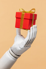 a bionic prosthetic arm or forearm in white on a beige background holds a red gift, prosthetics of...