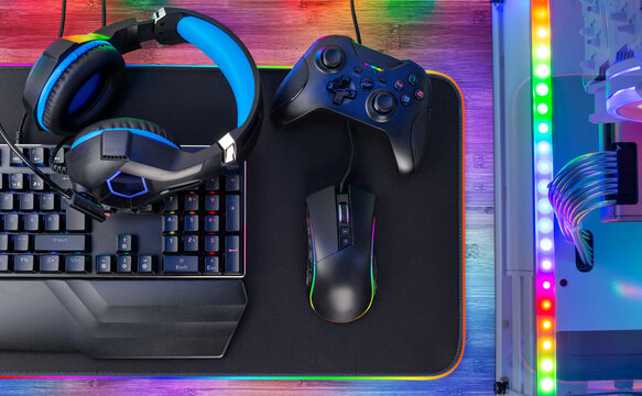 Top view of colorful bright pc rgb LED gaming desk with headset keyboard mouse and desktop computer.  esports technology concept background