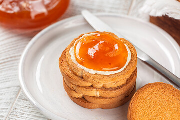 Close-up of Apricot Jam and Butter on Rusks or Fette Biscottate or Zwieback, toasted round Bread. High angle view. White table surface.