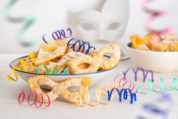 Carnival mask shape pastry Angel wings or sfrappole or chiacchiere. Traditional sweet crisp dessert deep-fried and sprinkled with powdered sugar. Decorated with paper serpentine. White background. - obrazy, fototapety, plakaty