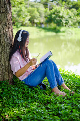 Woman reading a book in the park,Beautiful young woman sitting in autumn leaves under tree in woods or park listening music and day dreaming with book in hand 