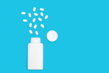 White pills for treatment with bottle on blue background, pharmacy and medicine concept, top view
