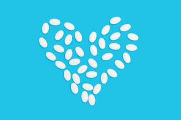 White pills for treatment in heart shape on blue background, pharmacy and medicine concept, top view