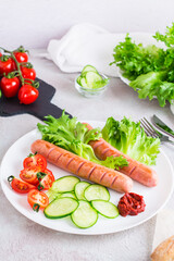 Ready-to-eat fried sausages and fresh vegetables on a plate on the table. Hearty homemade snack. Vertical view