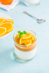 Homemade panna cotta with orange and mint leaf in a glass on a light table. Sweet Italian dessert. Vertical view. Close-up