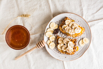 Ready to eat sandwiches with honey, banana and chocolate on a plate and honey on the table. Homemade vegetarian snack. Top view