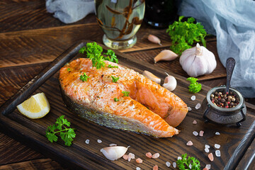 Baked salmon steak with herbs on wooden cutting board. Grilled salmon with salt and pepper