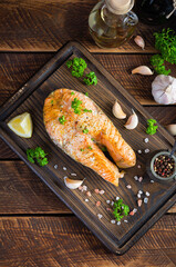 Baked salmon steak with herbs on wooden cutting board. Grilled salmon with salt and pepper