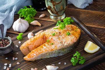 Baked salmon steak with herbs on wooden cutting board. Grilled salmon with salt and pepper